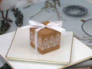 Square kraft paper candy box with white lace print and satin ribbon on golden plates