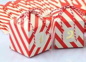 Detail van rood-wit gestreepte adventdoosjes met gouden cijferstickers en bindtouwtjes