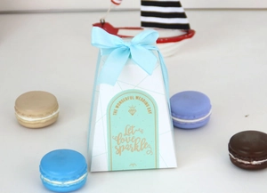 Detail der weißen Gastgeschenkbox mit blauer Schleife und mintgrünem Goldfolienetikett