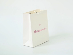 Detail view of cream white paper gift bag with pink The Bridesmaid lettering and cord handles