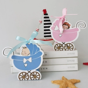 Pink and blue baby stroller shaped candy boxes with ribbon bows on a clean desk