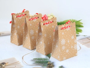 Set di quattro sacchetti regalo di Natale in carta kraft con fiocchi di neve e nastri rossi