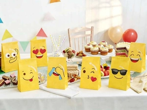 Detail of yellow emoji paper gift bags on a party table with cakes and balloons
