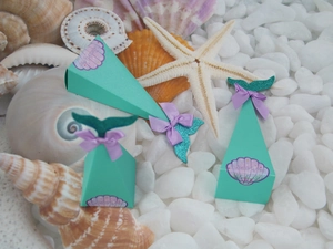 Close-up of mermaid candy boxes with purple ribbons and shells on seashells background