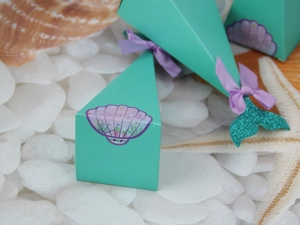 Detail view of mermaid party favor boxes with sea shells and starfish on white pebbles