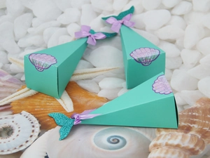 Detail of mermaid-themed gift box with silk bow, fish tail, and shells on pebbles