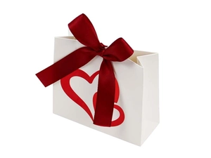 Close-up of white gift bag featuring red heart patterns and a satin crimson bow detail