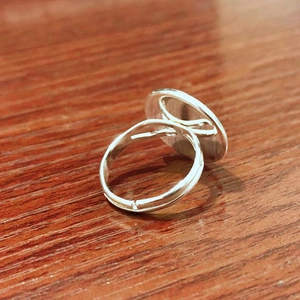 Polished silver adjustable ring with flat circular top on a textured wood surface