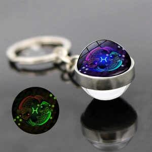 Detailed view of luminous Pisces constellation glass ball keychain with glowing green effect