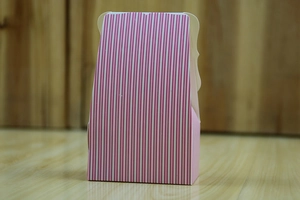 Detail of pink and white striped trapezoid wedding candy box on light wood surface