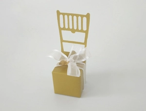 Detail of golden chair-shaped wedding favor box with white ribbon and heart charm