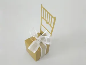 Detail of a gold chair-shaped gift box featuring a white organza ribbon and heart charm