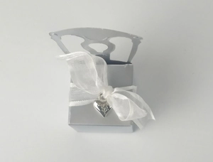 Detail of silver chair-shaped candy box with white organza ribbon and engraved heart pendant