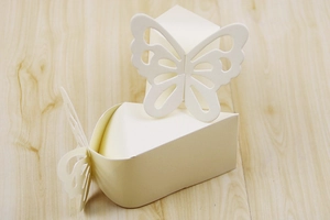 Detail of laser-cut butterfly hollow candy boxes in ivory white paper on wooden surface