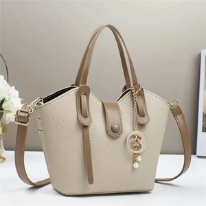 Borsa a secchiello beige con manici marroni e ciondolo stella-luna dorato su sfondo soft