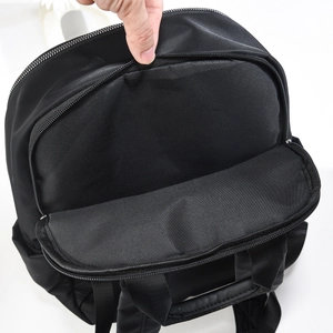 Top detail of black nylon backpack featuring reinforced handle and metal double zippers