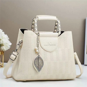 Detail of cream plaid bucket bag featuring metal leaf pendant and woven chain handle