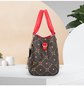 Detail of dark brown leather tote with red handles and gold pearl chain charm