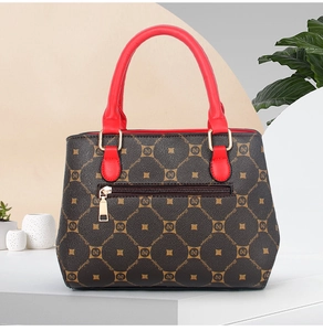 Detailed view of luxury printed handbag with red leather handles and gold zipper hardware