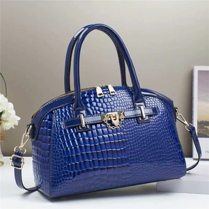 Sac à main bleu foncé motif crocodile avec fermoir doré et poignées sur socle blanc