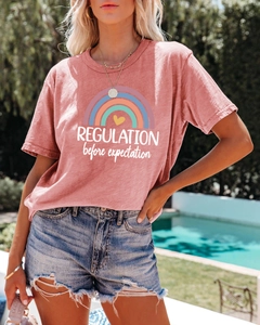Outdoor shot of a pink cotton T-shirt featuring rainbow print and Regulation text detail