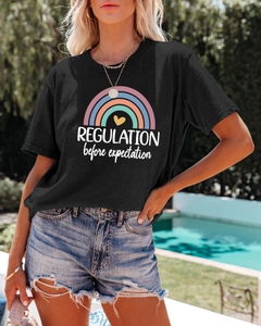 Detail of black cotton T-shirt featuring rainbow print and slogan in outdoor summer setting
