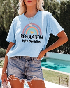Detail of light blue t-shirt featuring rainbow print and 'REGULATION before expectation' text