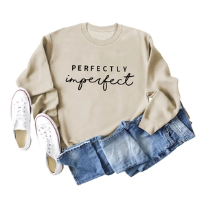 Sweat-shirt beige col rond avec imprimé PERFECTLY imperfect posé à plat avec un jean