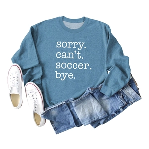 Flat lay of blue sweatshirt with 'Sorry Can't Soccer Bye' text and denim shorts outfit