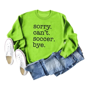 Flat lay of neon green soccer sweatshirt with Sorry Can't Soccer Bye text and casual items