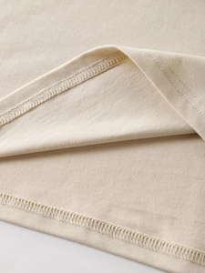 Close-up of double-needle hem stitching and fine fabric texture on beige cotton t-shirt