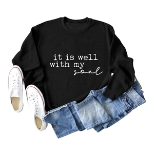 Flat lay of a black crewneck sweatshirt with 'it is well with my soul' text and jeans