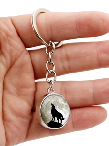 Close-up of a silver keychain featuring a howling wolf and full moon glass pendant