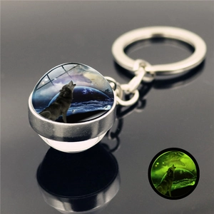 Detail of howling wolf glass ball keychain with glowing green moonlight effect in darkness