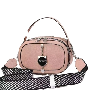 Pink oval crossbody bag with textured leather and a cat pendant on wide strap