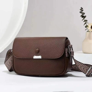 Brown lychee leather crossbody bag with wide patterned strap on white background