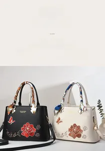 Dettaglio borsa ricamata a fiori nera e beige con manico decorato da foulard in seta