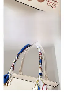 Dettaglio dell'elegante ricamo floreale e della sciarpa di seta sulla borsa color crema