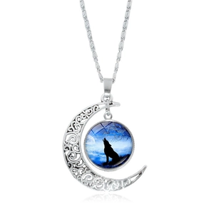 Détail d'un pendentif lune évidé argenté avec ciel bleu et silhouette de loup hurlant