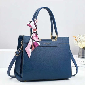 Detail of navy blue bucket bag with gold logo and decorative printed silk scarf on handle