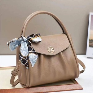 Detail view of coffee-colored lychee leather texture and golden metal M-logo on the handbag