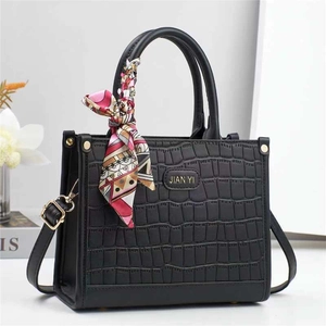 Elegante borsa nera con stampa coccodrillo, foulard di seta e logo dorato sulla scrivania
