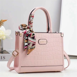 Dettaglio borsa a mano rosa con trama a coccodrillo e foulard decorativo in seta sul manico