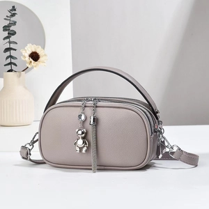 Detail of gray-purple crossbody bag with twin zippers and luxury tassel bear charm