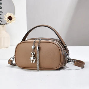 Detail of khaki round leather handbag with twin zippers and metal bear charm accessory
