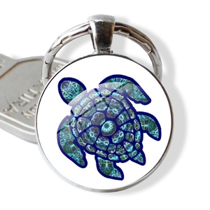 Détail d'un porte-clés tortue argenté rond avec motif mandala coloré et dôme en verre