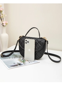 Detail view of black quilted shell bag with gold hardware next to a phone for size scaling
