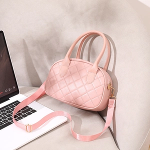 Pink quilted shell-shaped handbag with adjustable strap shown on a sofa next to a laptop