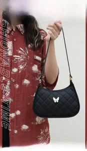 Detail of black quilted crescent bag with white butterfly metal ornament and strap