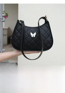 Detail of black quilted shoulder bag featuring a white butterfly buckle and hobo design